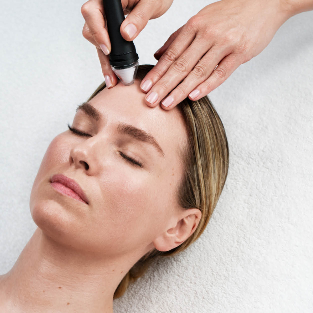 Frau mit geschlossenen Augen, liegend bei einer Gesichtsbehandlung mit Apparat.